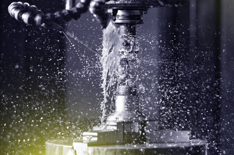 Spindle chuck and installed metal part in pocessing on high precision Cnc industrial lathe turning machine. CNC machine drills a hole in a metal part Close up. Lots of coolant spray