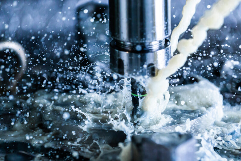 Close up view of vertical cnc steel milling process with external water coolant streams, splashes and a lot of metal chips, high contrast